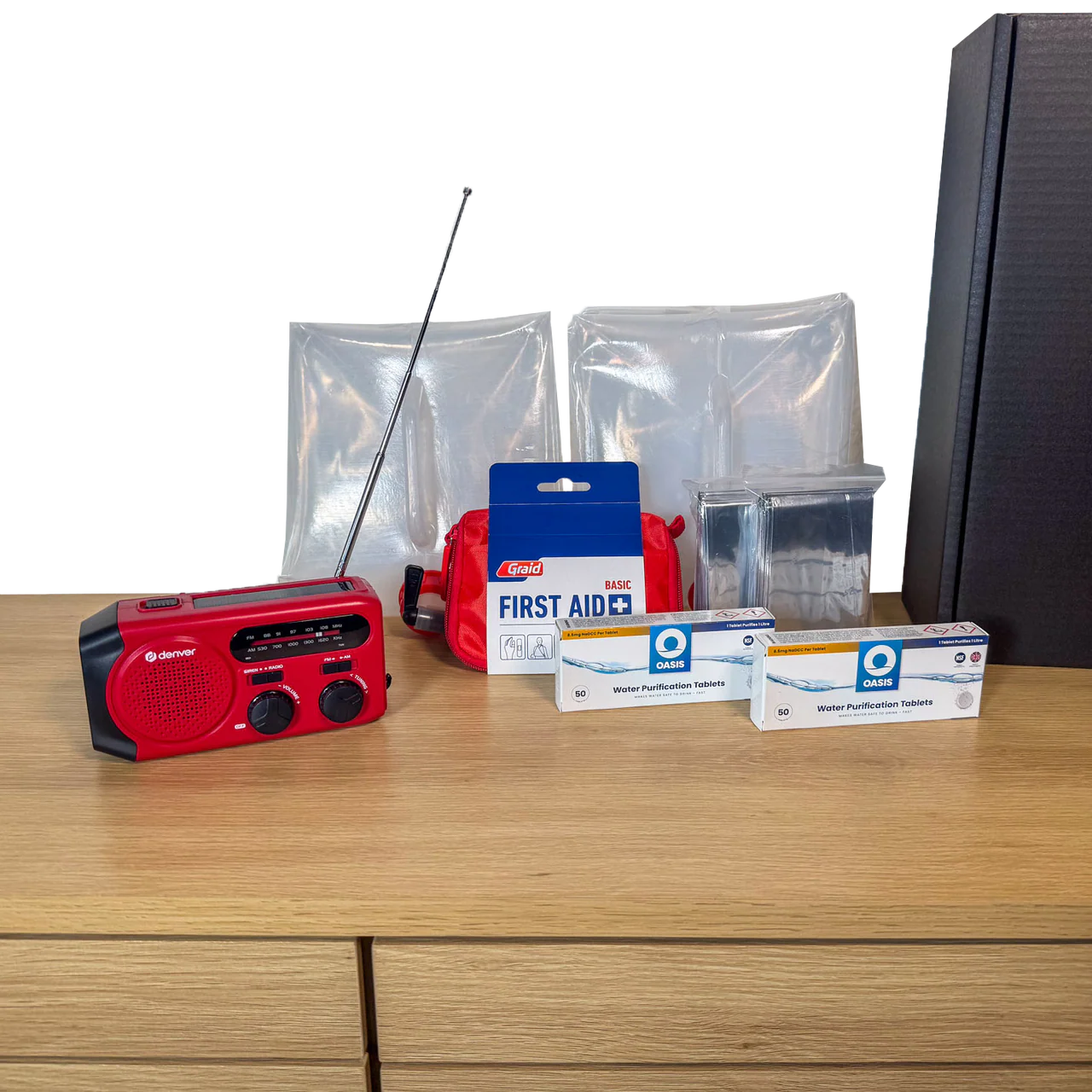 Udpakket PrepBox Essentials med nødradio, førstehjælpssæt, nødtæpper, vandrensningstabletter og sort opbevaringsæske.