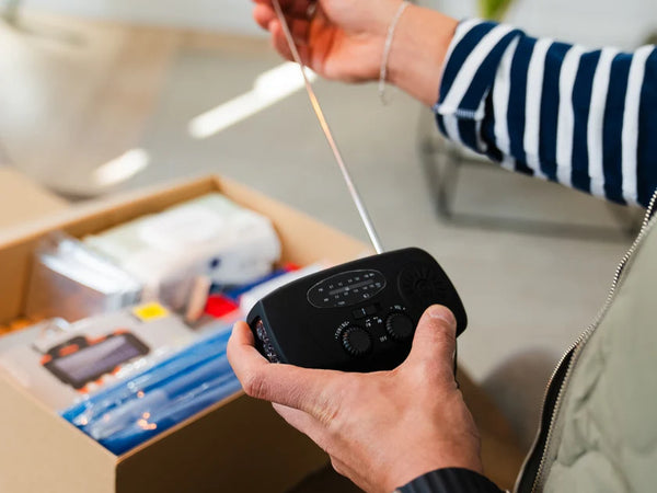 Person holder en nødradio fra PrepBox med antennen trukket ud, mens en åben beredskabskasse står på bordet i baggrunden.